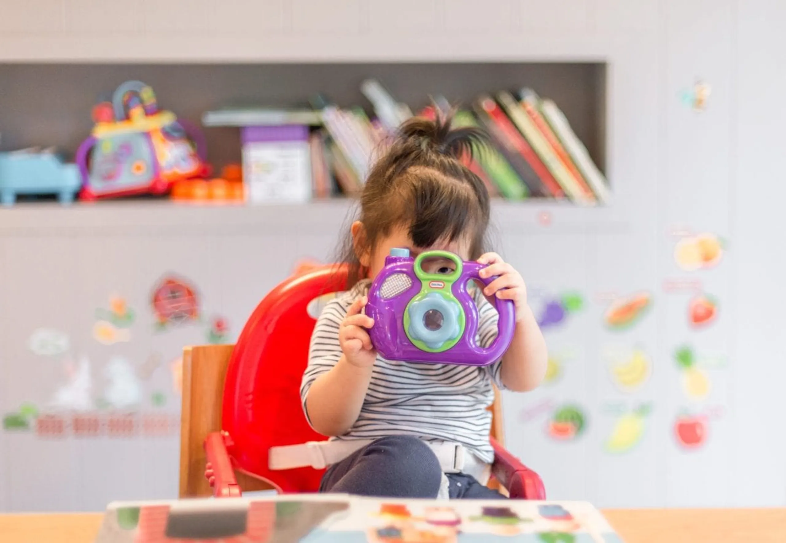 Child holding a toy camera in a classroom