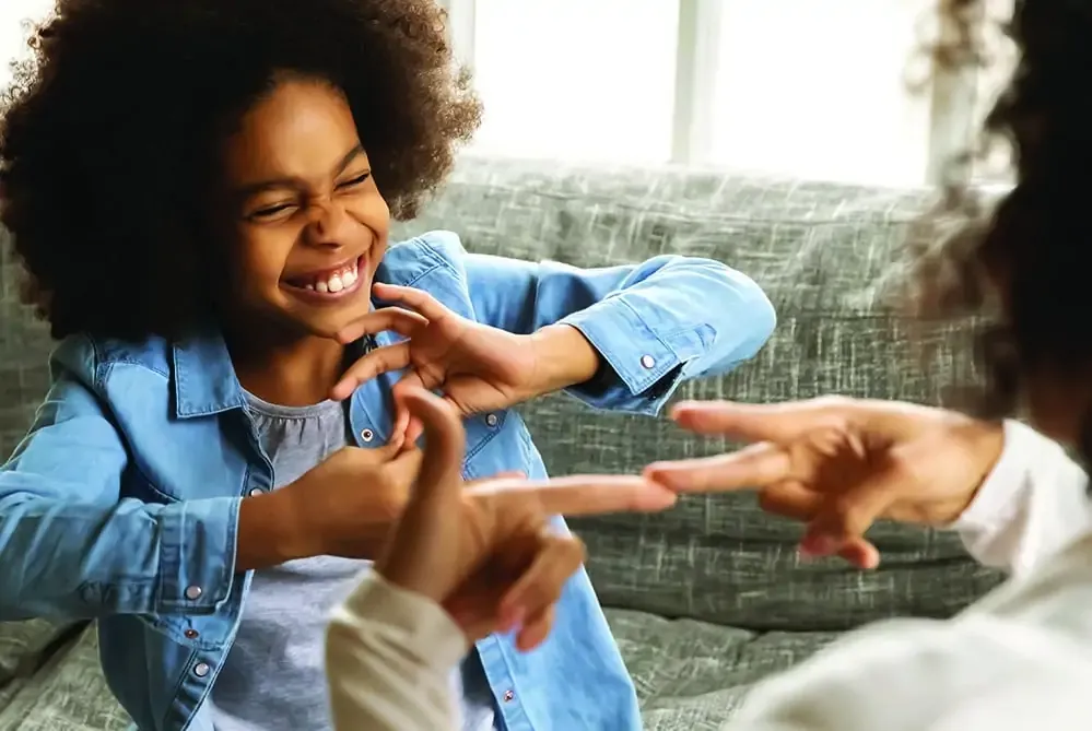 A child smiling while learning sign language with a caregiver